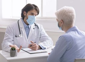 Arzt spricht mit Patientin und beide tragen eine Maske