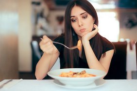 eine junge Frau sitzt appetitlos vor einem Teller Nudeln mit Sugo
